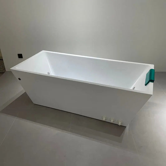The Deluxe Plunge by Lunara is a modern rectangular white bathtub with clean lines and durable design, featuring a green headrest and three side control knobs. It’s shown on gray tiles against a plain light wall.